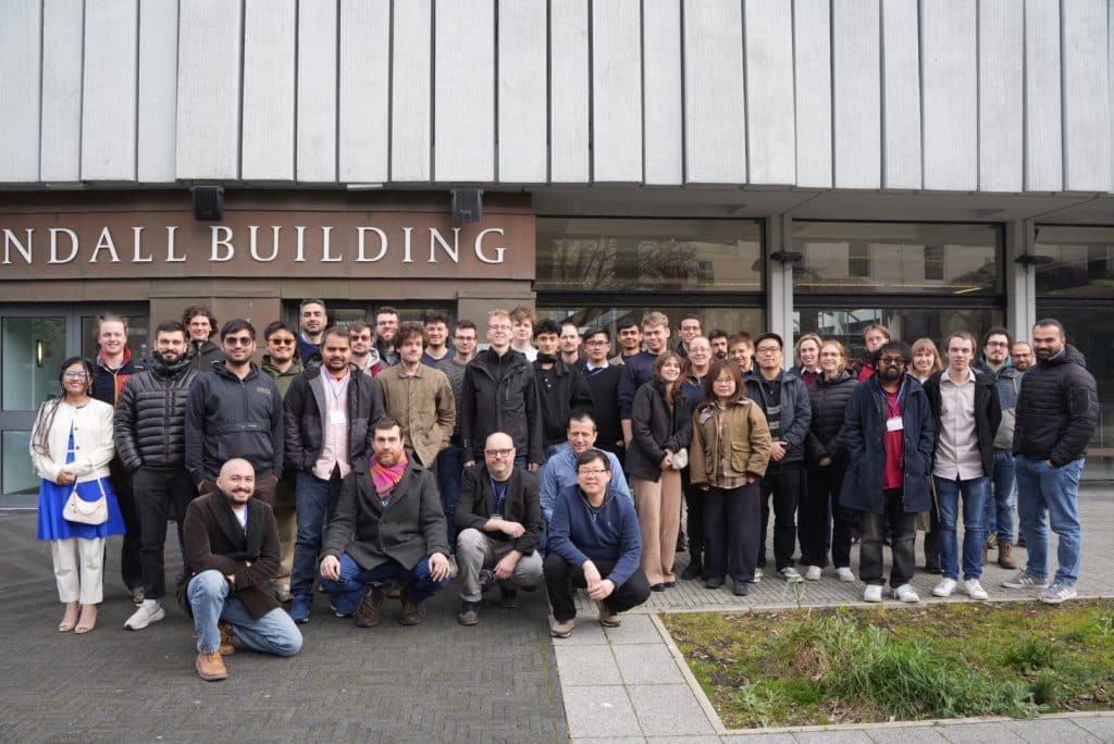 The image is a group photo of around 40 people. These people are participants of the LBM Spring School. They are standing in front of a building.